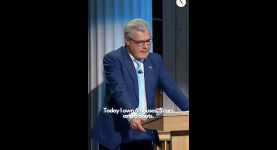 Reform leader Malcolm Offord stands at a podium, where he says he has six houses, six boats and five cars